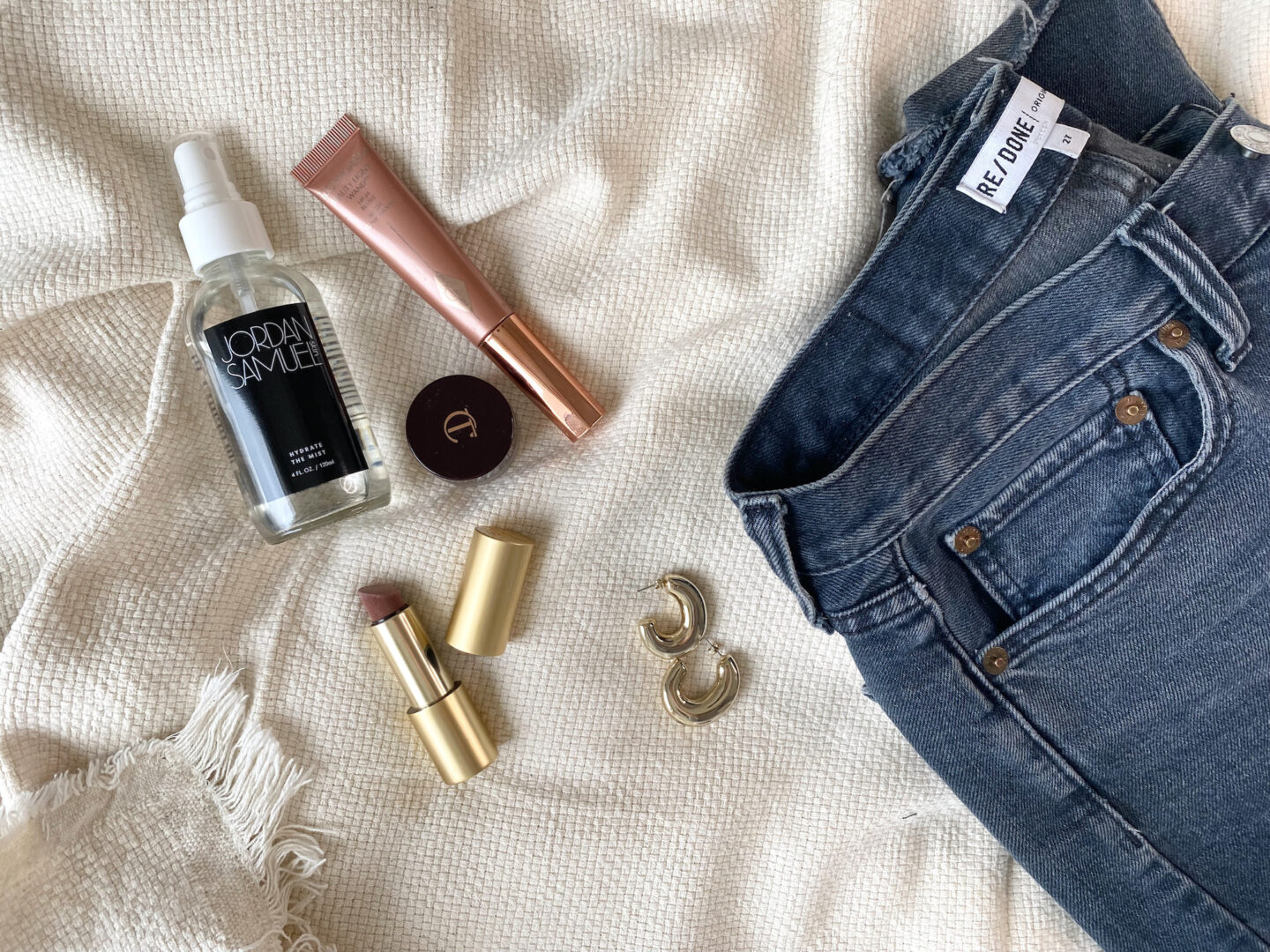Makeup products along with a pair of jeans and earrings to get ready